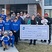 Boys little league baseball team standing outside office building with large check for $1,000